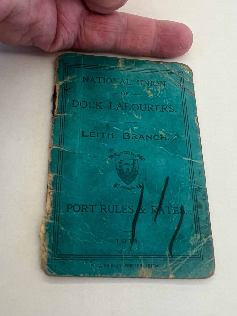 Turquoise booklet with a man's finger at the top showing size reference. 