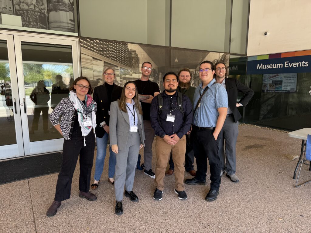 A group of 7 people posing together in front of double doors.